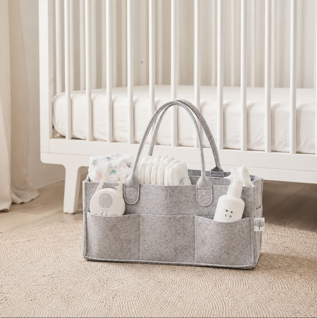 Light gray baby organiser with items in front of a white cot in a nursery.