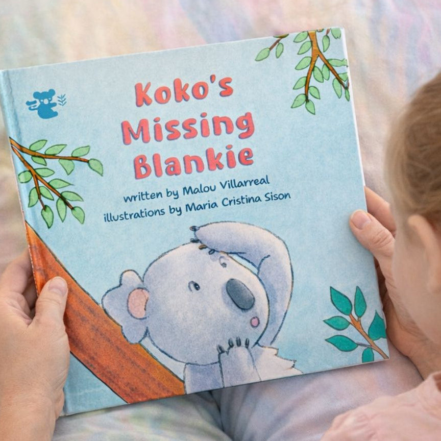 Child reading a book titled 'Koko's Missing Blankie' with a koala illustration on a bed.