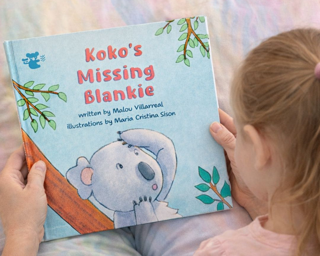 Child reading a book titled 'Koko's Missing Blankie' with a koala illustration on a bed.